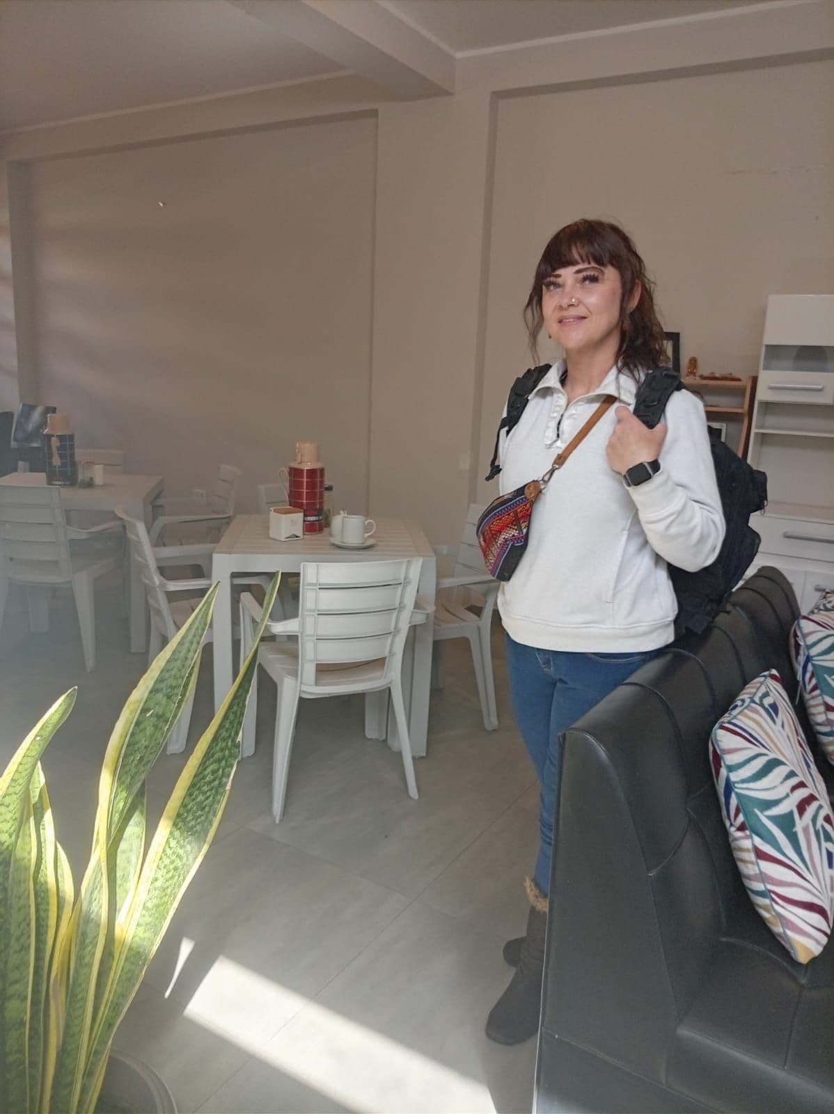 A person standing in a room with a dining area, a sofa, and a plant.