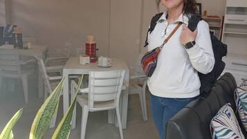 A person standing in a room with a dining area, a sofa, and a plant.