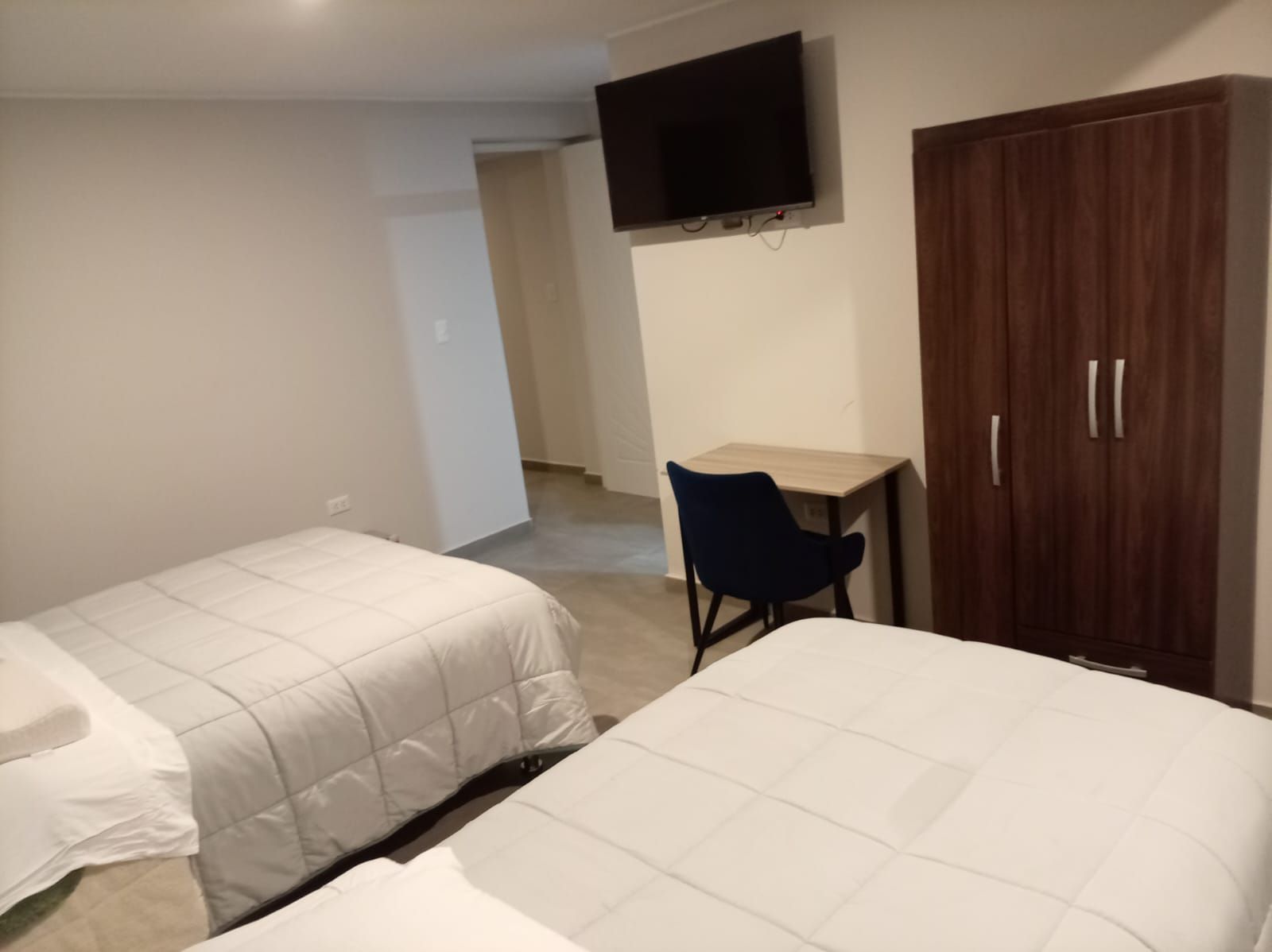 A hotel room with two beds, a desk, a chair, a wardrobe, and a television on the wall.