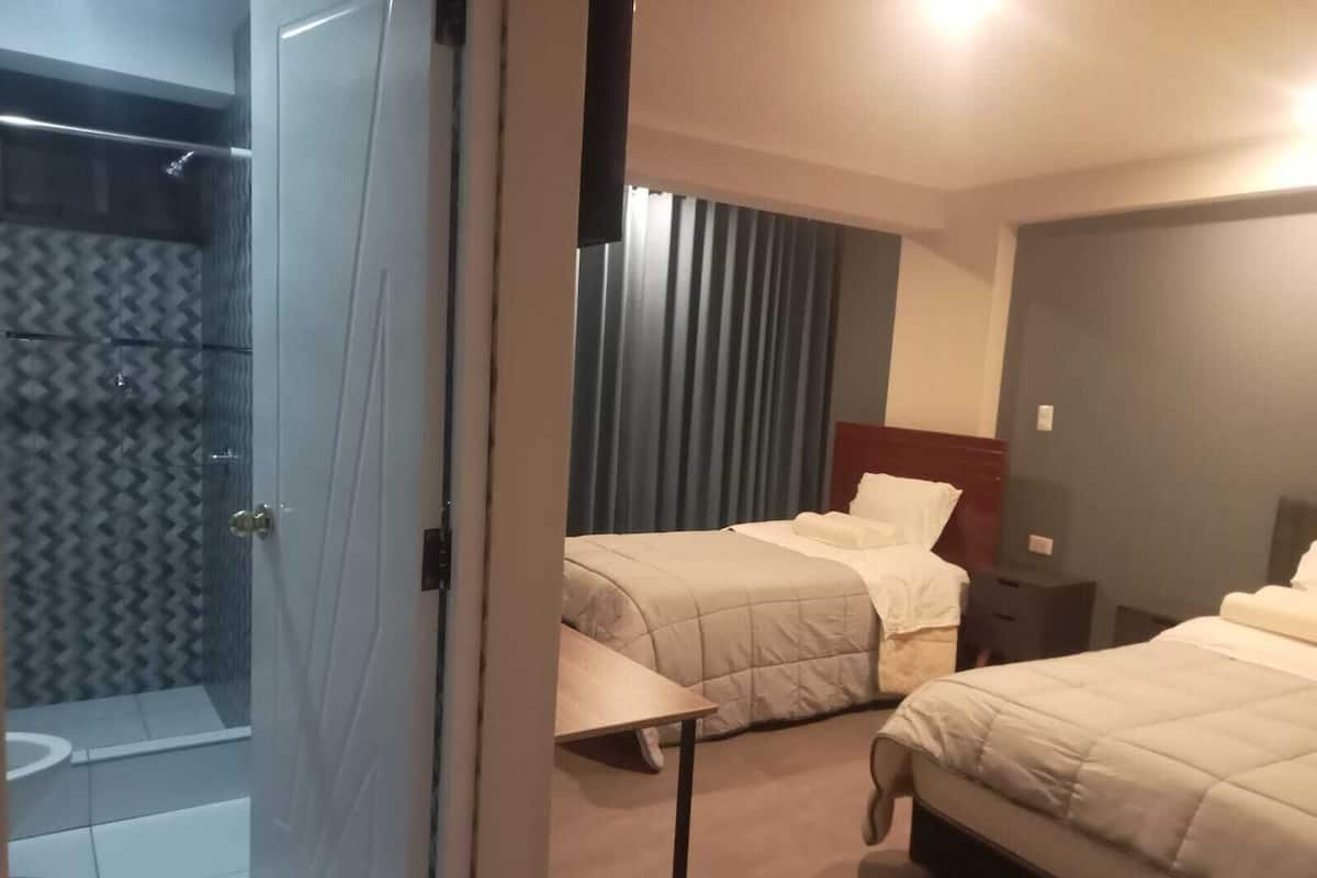 A hotel room with two beds, a shower, and a small table.