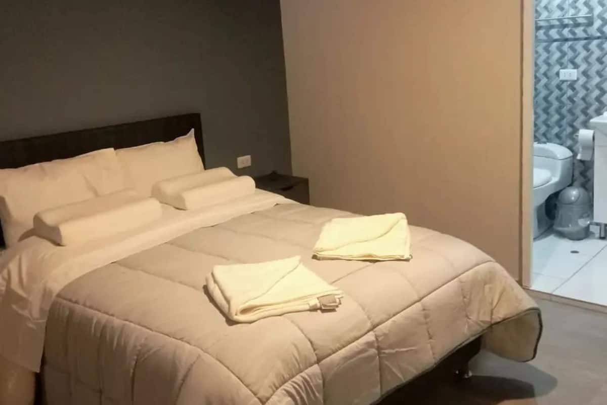 A neatly made bed with white linens and a beige quilted duvet.