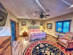 Ein Schlafzimmer mit Bett, Deckenventilator, Fenster mit Jalousien, Stuhl und Teppich.