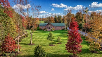 A lodge with a green roof, surrounded by a well-maintained lawn and trees with autumn foliage.