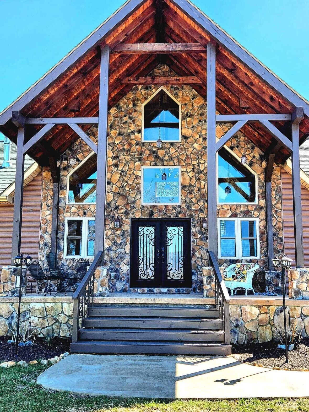 Ein Steinhaus mit einer hölzernen Veranda, einer schwarzen Tür mit schmiedeeisernen Verzierungen und einer Steintreppe, die zum Eingang führt.
