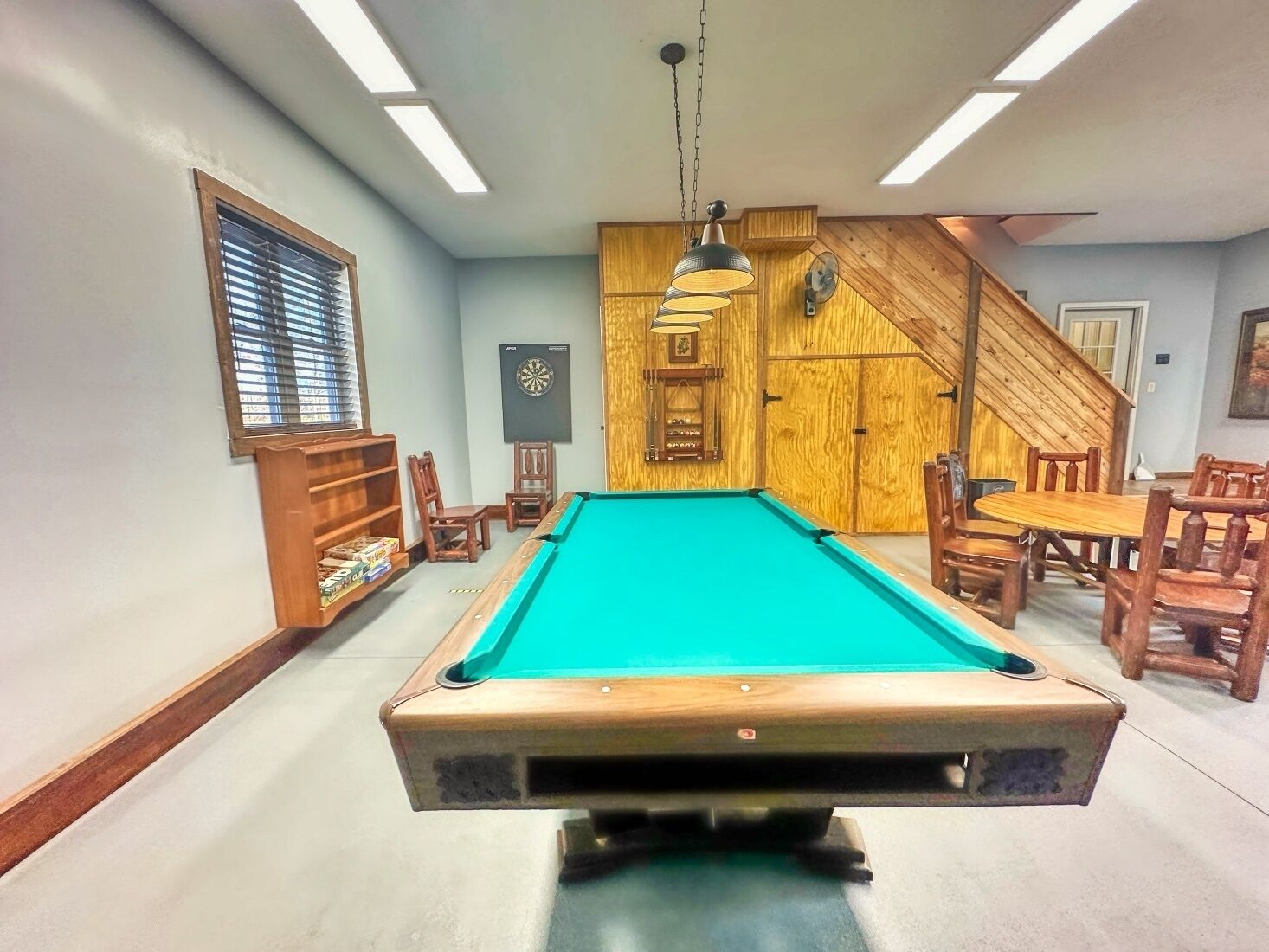 A pool table in a room with wooden walls, a staircase, and a dartboard.