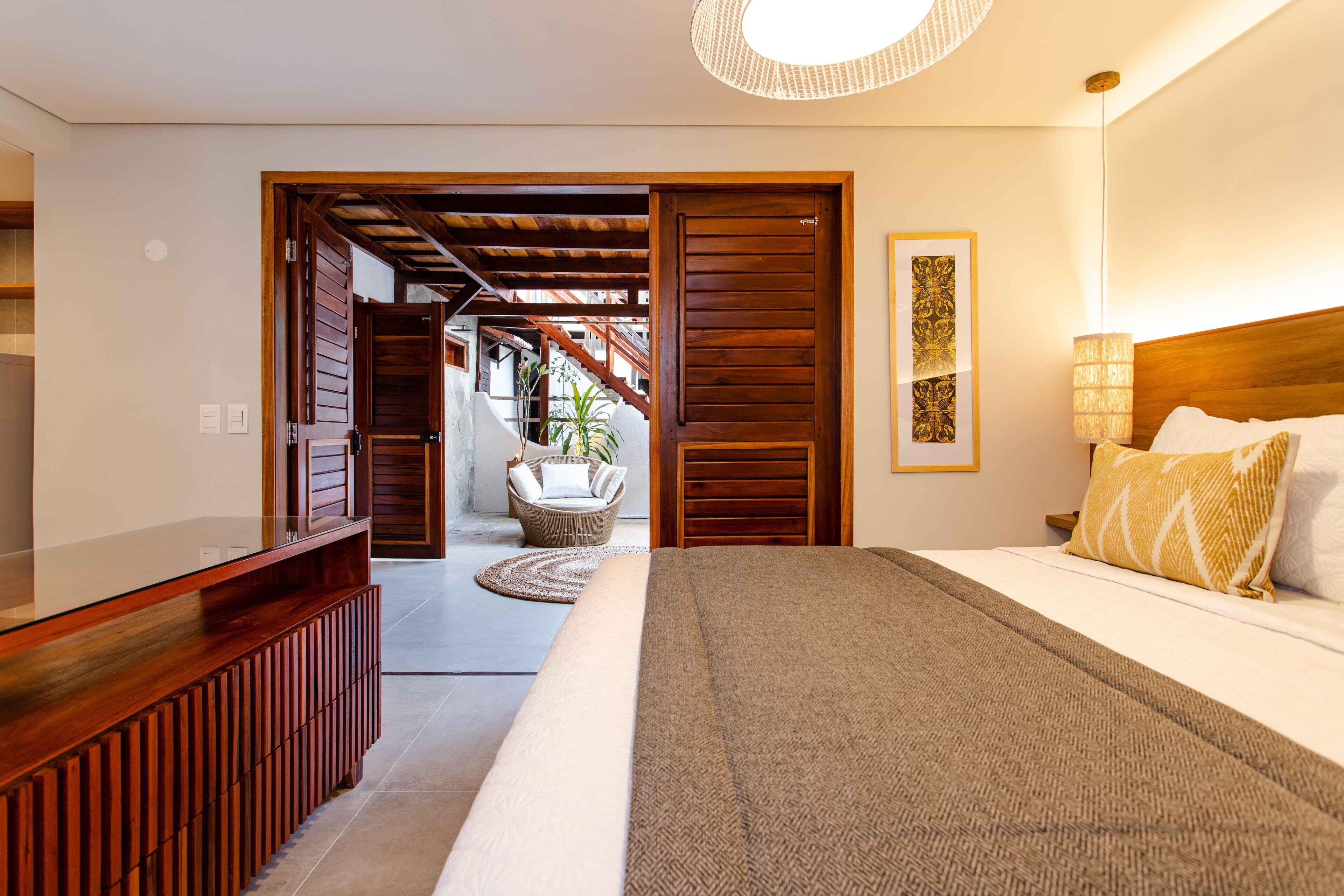 A bedroom with a large bed, wooden headboard, and a bedside lamp. There is a chair and a small table in the corner.