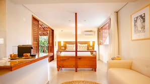 A bedroom with a wooden bed, a sofa, a woven rug, and a small table with a television and bowls. - Villa Nanui Jeri (Jijoca de Jericoacoara)