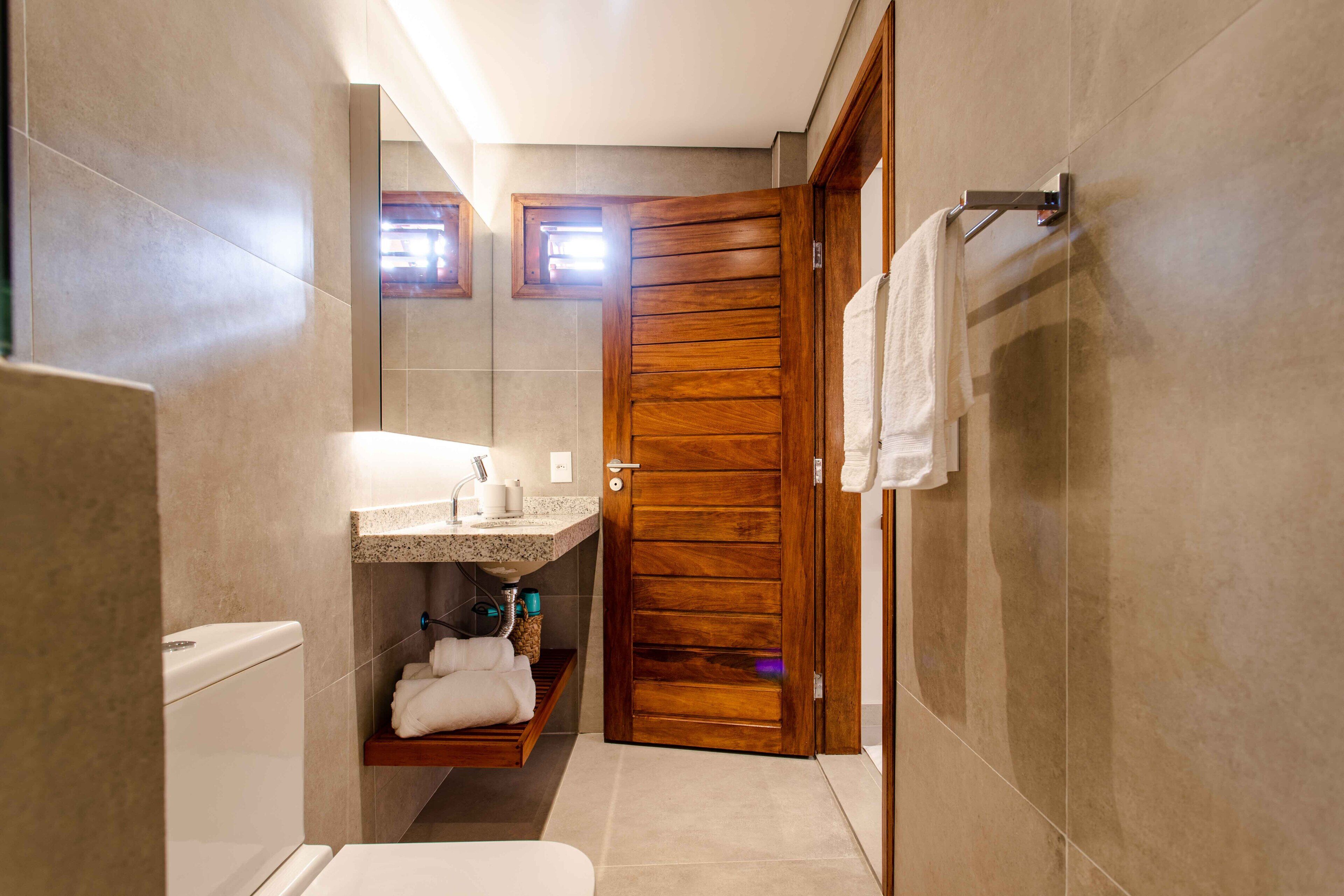A modern bathroom with a wooden door, a toilet, a sink with a countertop, and a shelf with towels.
