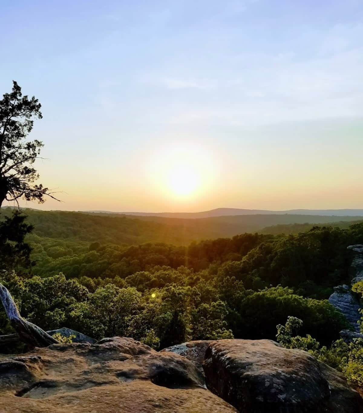 A natural landscape with a sunlit sky, dense greenery, and rocky terrain.