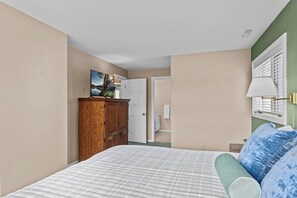 Une chambre à coucher avec un lit, une armoire en bois, un tableau et une fenêtre avec des stores.