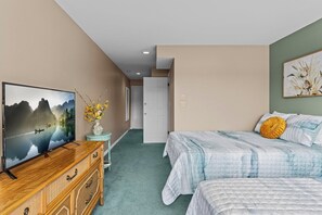 Une chambre avec une télévision, une commode, un lit avec des oreillers, un vase de fleurs et un tableau au mur.