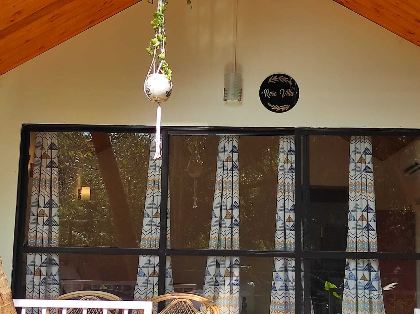 A window with patterned curtains, a hanging light fixture, and a sign that reads "Rose Villa".