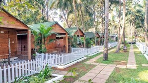 Wooden cabins with green roofs, white picket fences, and a paved walkway surrounded by lush greenery. - Kings Villa Resort (Canacona)