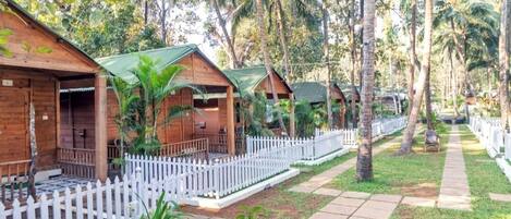 Wooden cabins with green roofs, white picket fences, and a paved walkway surrounded by lush greenery.