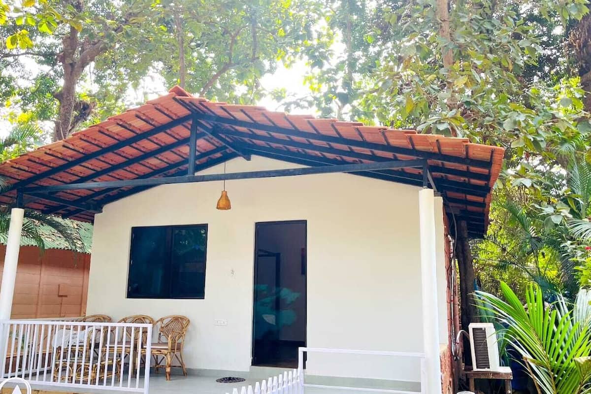 A single-story building with a tiled roof, a white exterior, and a porch with wicker furniture.