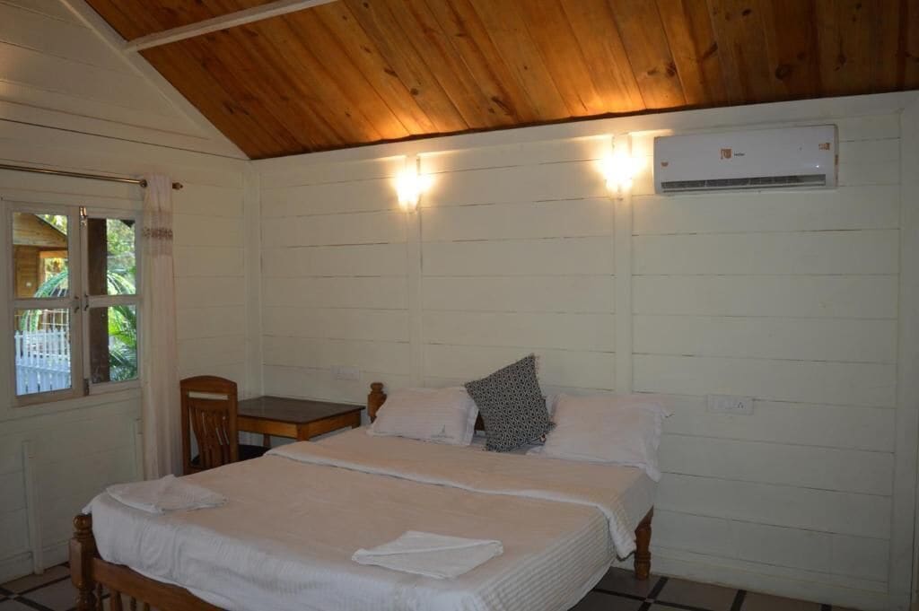 A single-bed room with a wooden ceiling, white walls, and an air conditioning unit.