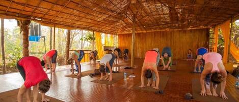 Un grupo de personas practicando yoga en una habitación con techo de paja y paredes de madera.