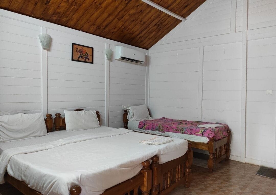 A bedroom with two wooden beds, white walls, a wooden ceiling, a small table, and a wall-mounted air conditioner.
