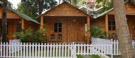 A row of wooden cabins with a white picket fence in front, surrounded by lush greenery.