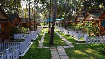 A row of wooden cabins with white picket fences, surrounded by lush greenery and palm trees.