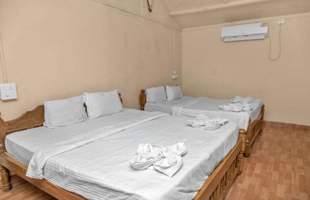 A room with two wooden beds, each with a white bedspread and pillows. There are towels on the beds.