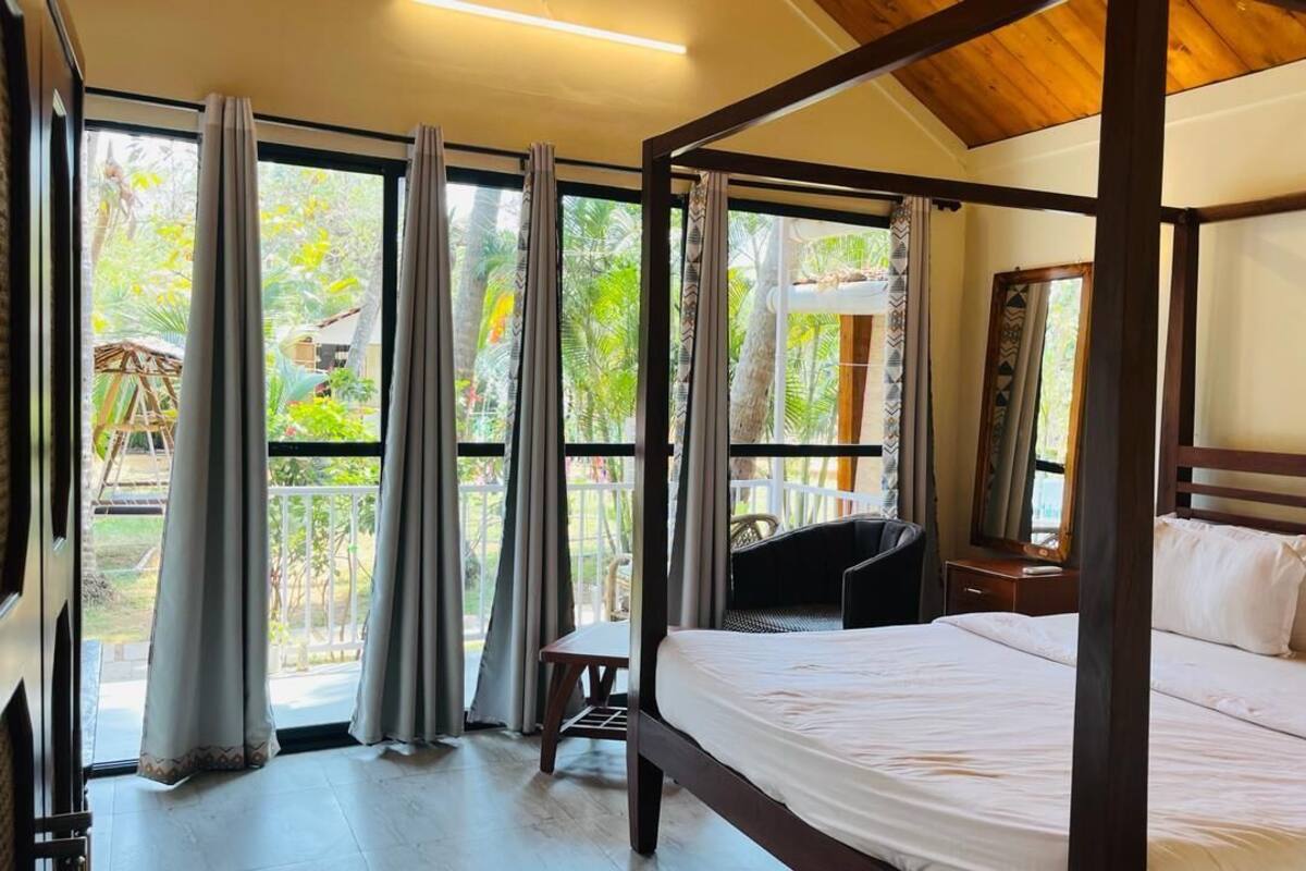 A bedroom with a large bed, a chair, a desk, and a window with curtains.