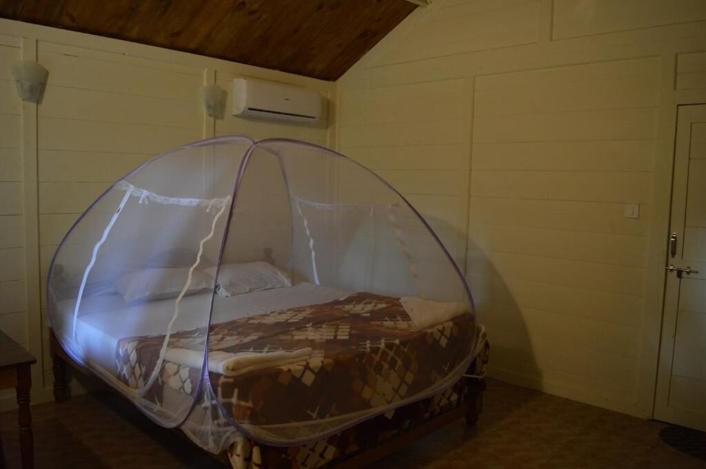 Un lit simple avec une moustiquaire, dans une pièce aux murs blancs et au plafond en bois.
