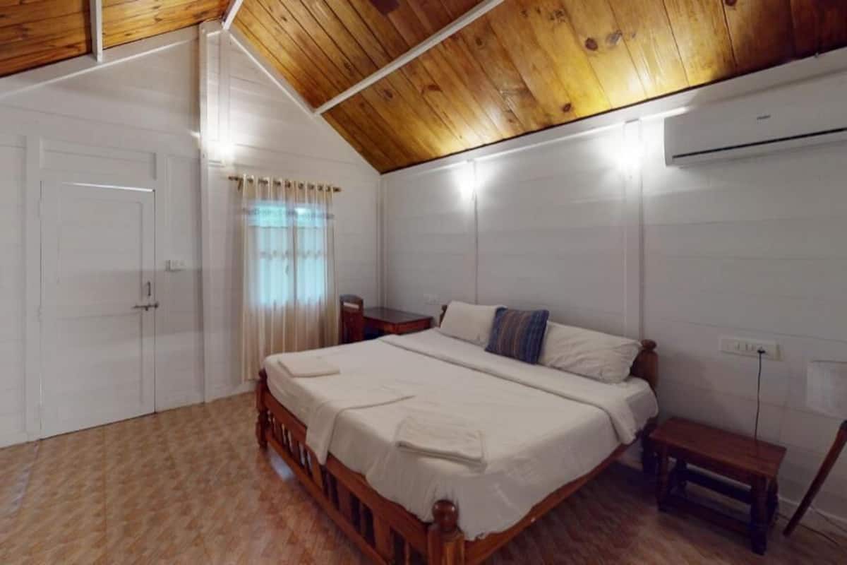 A bedroom with a wooden ceiling, a bed with white bedding, a bedside table, and a window with curtains.