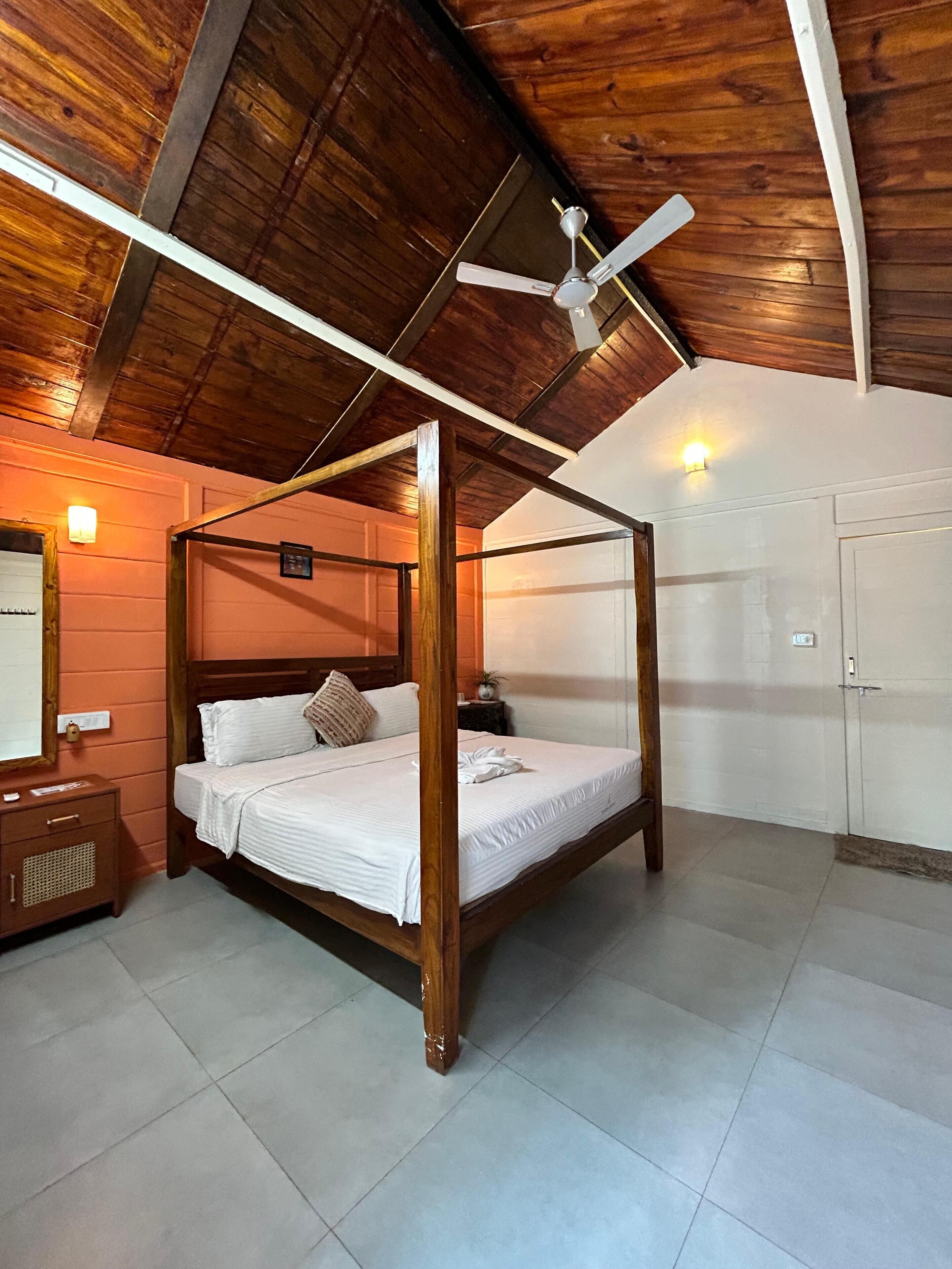 Una cama con dosel en una habitación con vigas de madera en el techo, un ventilador de techo y una puerta blanca.