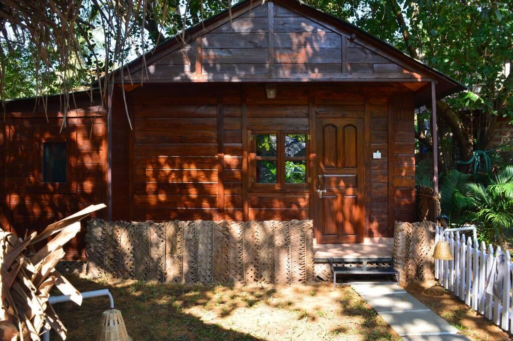 Une cabane en bois rustique, avec une porte d’entrée, un petit porche et une clôture en piquets.