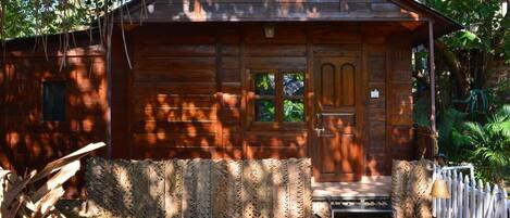 A rustic wooden cabin with a front door, a small porch, and a picket fence.