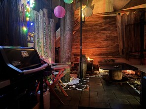 A rustic wooden interior with a grill, seating area, and decorative lights. -   Premium Stay Academy - Luxus-Ferienwohnungen mit Erlebnis (Bad Ems)