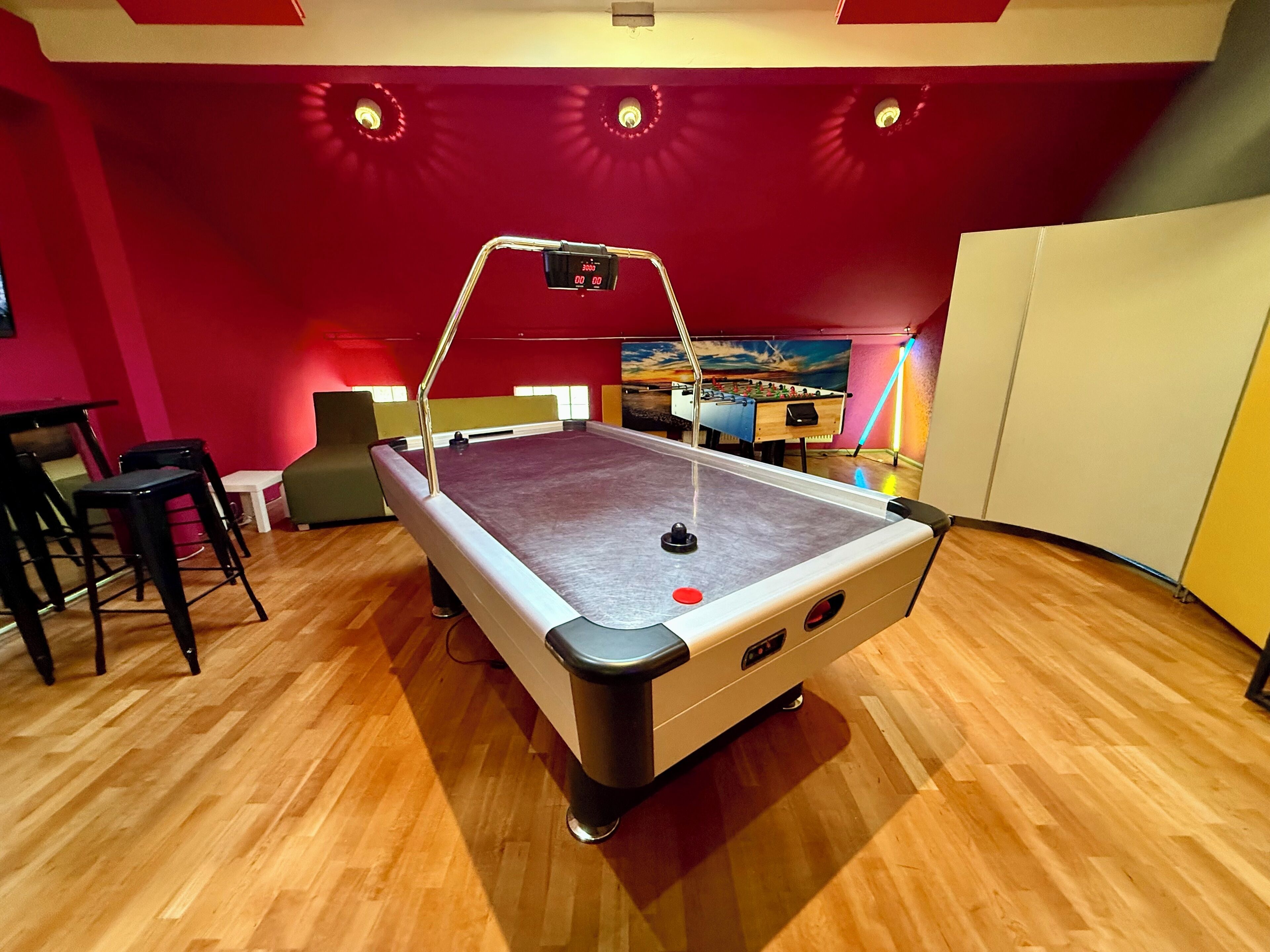 A pool table with a red wall and wooden flooring.
