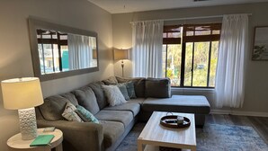 A living room with a sectional sofa, a round side table, a coffee table, and a window with curtains.