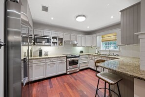 A modern kitchen with stainless steel appliances, white cabinetry, and a wooden floor.