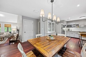 A spacious kitchen with white cabinets, a wooden dining table, and a chandelier.