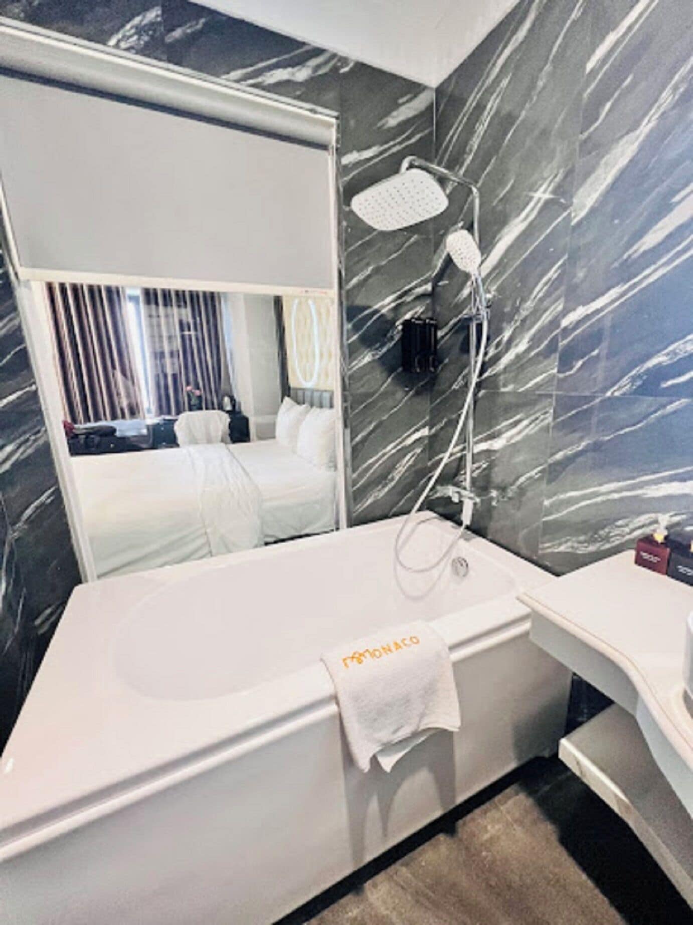 A modern bathroom with a marble backsplash, a large mirror, a shower with a handheld head, and a towel rack with a towel.