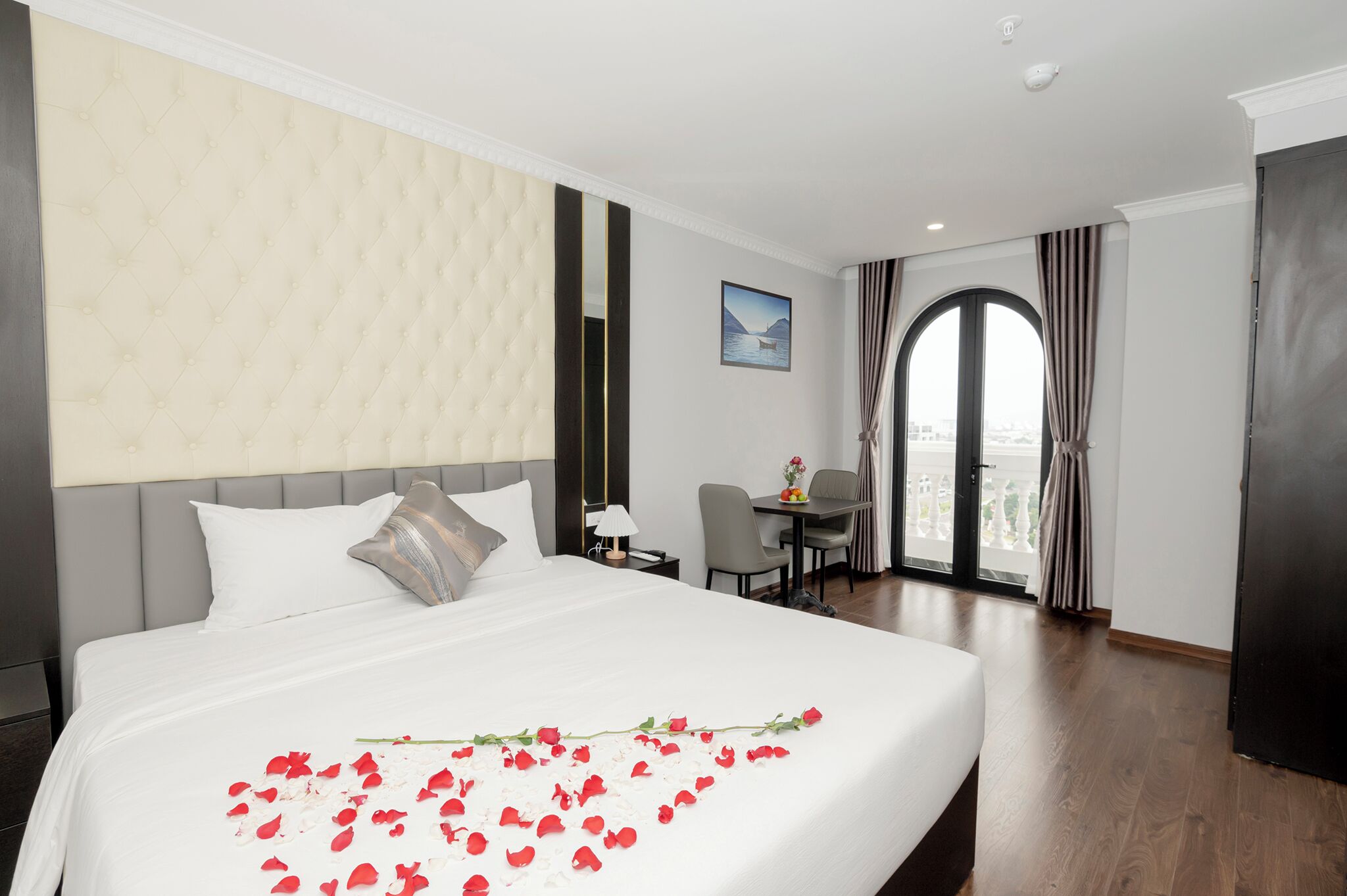 A hotel room with a large bed, a desk, and a view of the city through a large window.