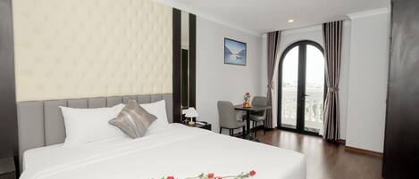 A hotel room with a large bed, a desk, and a view of the city through a large window.