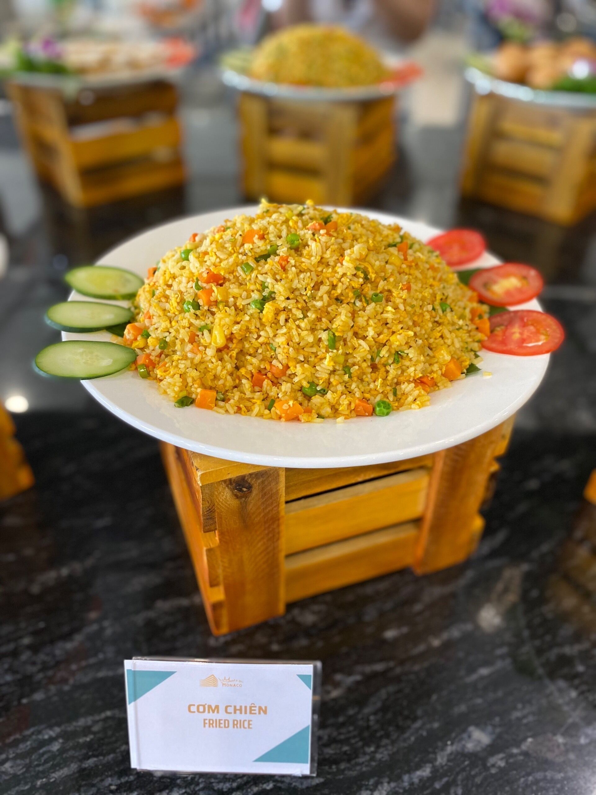 A large plate of fried rice with vegetables and cucumber slices on a wooden stand.