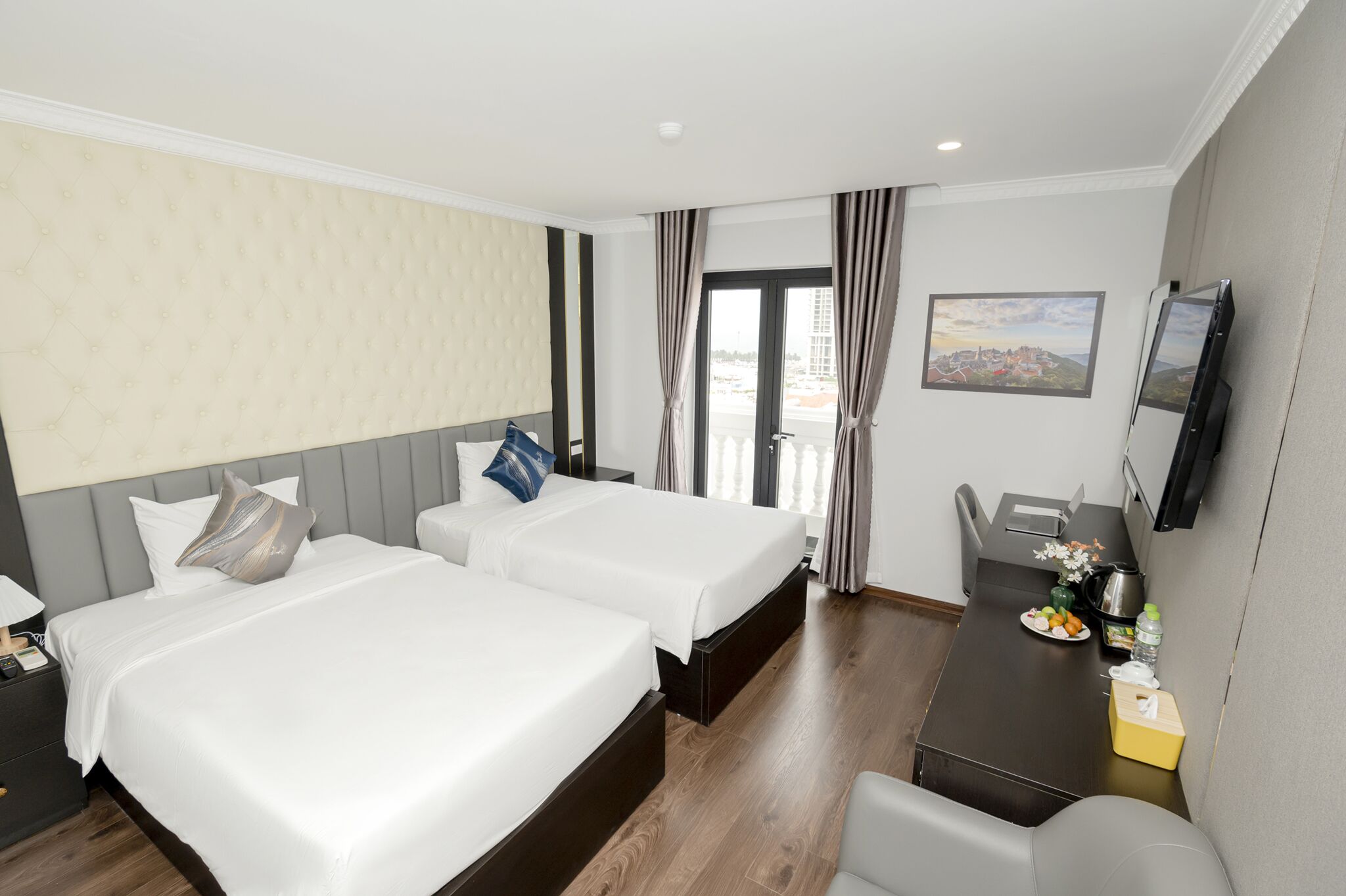 A hotel room with two beds, a desk, a chair, a TV, and a window with curtains.