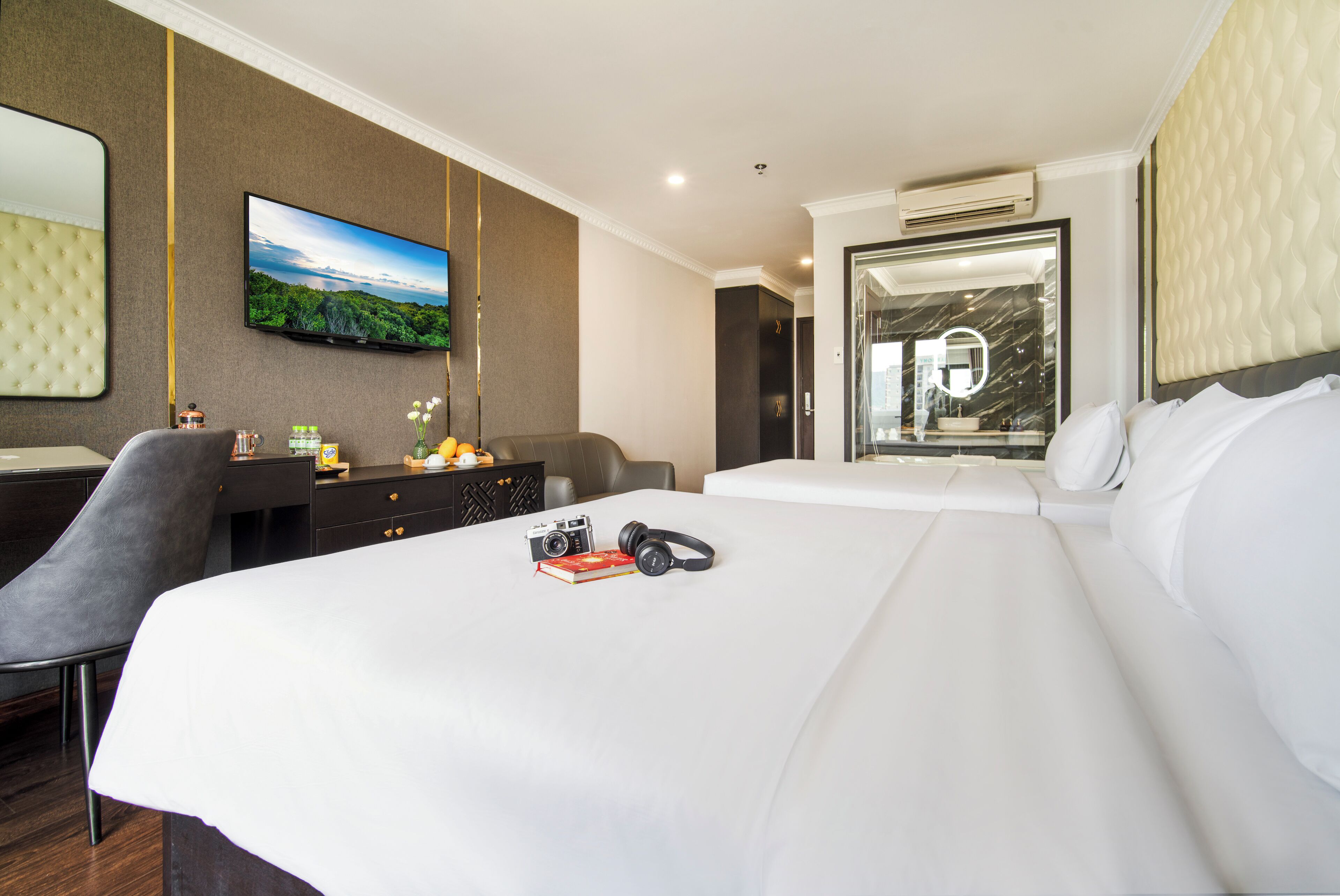 Habitación de hotel con una cama grande, un escritorio con silla, un televisor montado en la pared y un baño visible a través de una puerta abierta.