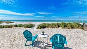 A beachside table with two chairs and a bottle of wine, overlooking a sandy beach with grass and a clear blue sky. - Fins to the Right: On the Gulf of Mexico! Beach! (Holmes Beach)