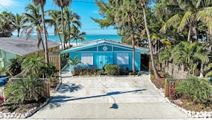 A blue house with a front porch, surrounded by palm trees and a clear sky. - Fins to the Right: On the Gulf of Mexico! Beach! (Holmes Beach)