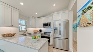 A modern kitchen with white cabinetry, stainless steel appliances, and a marble countertop. - Fins to the Right: On the Gulf of Mexico! Beach! (Holmes Beach)