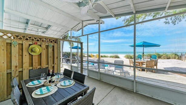 A covered patio with a table set for dining, overlooking a beach with umbrellas and chairs. - Fins to the Right: On the Gulf of Mexico! Beach! (Holmes Beach)
