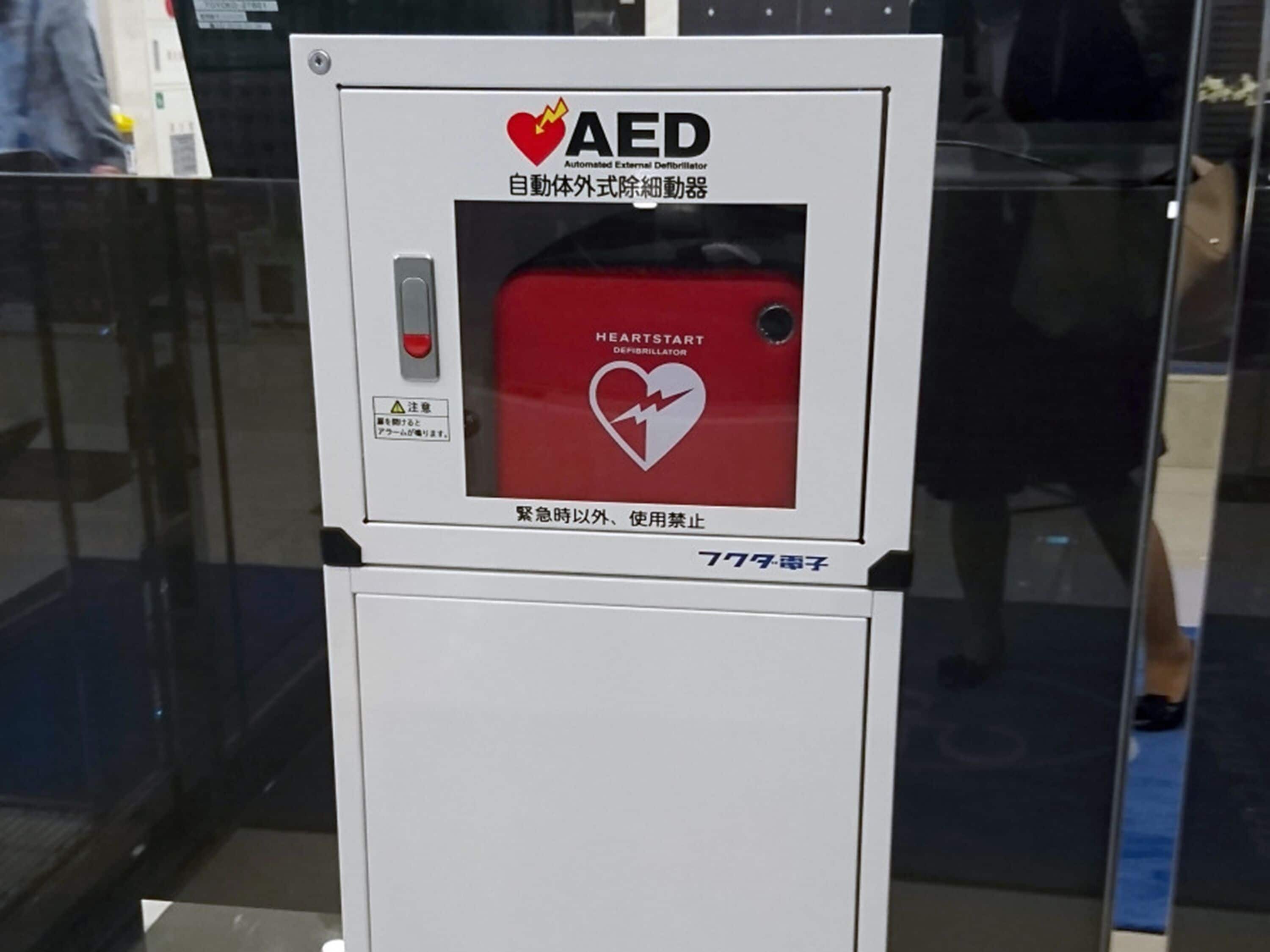 An AED device with a red panel and a heart symbol, labeled in both English and another language.