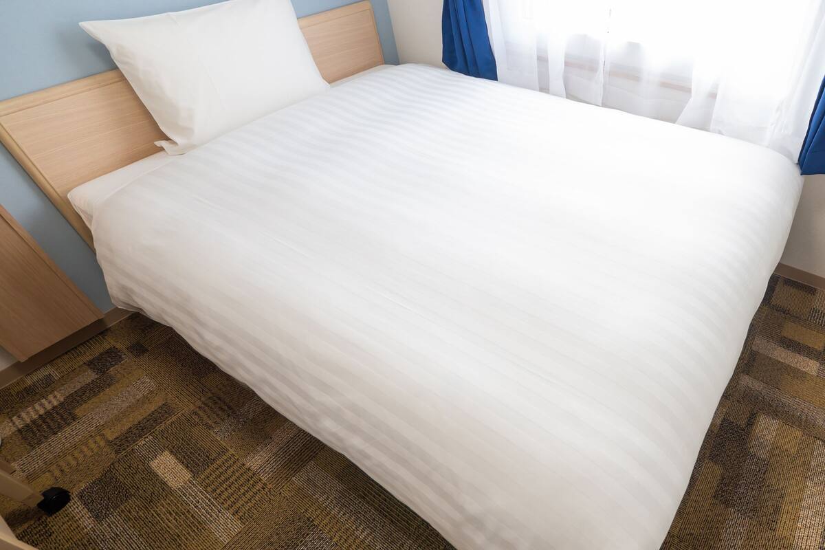 A neatly made bed with white bedding, a wooden headboard, and a patterned carpet.