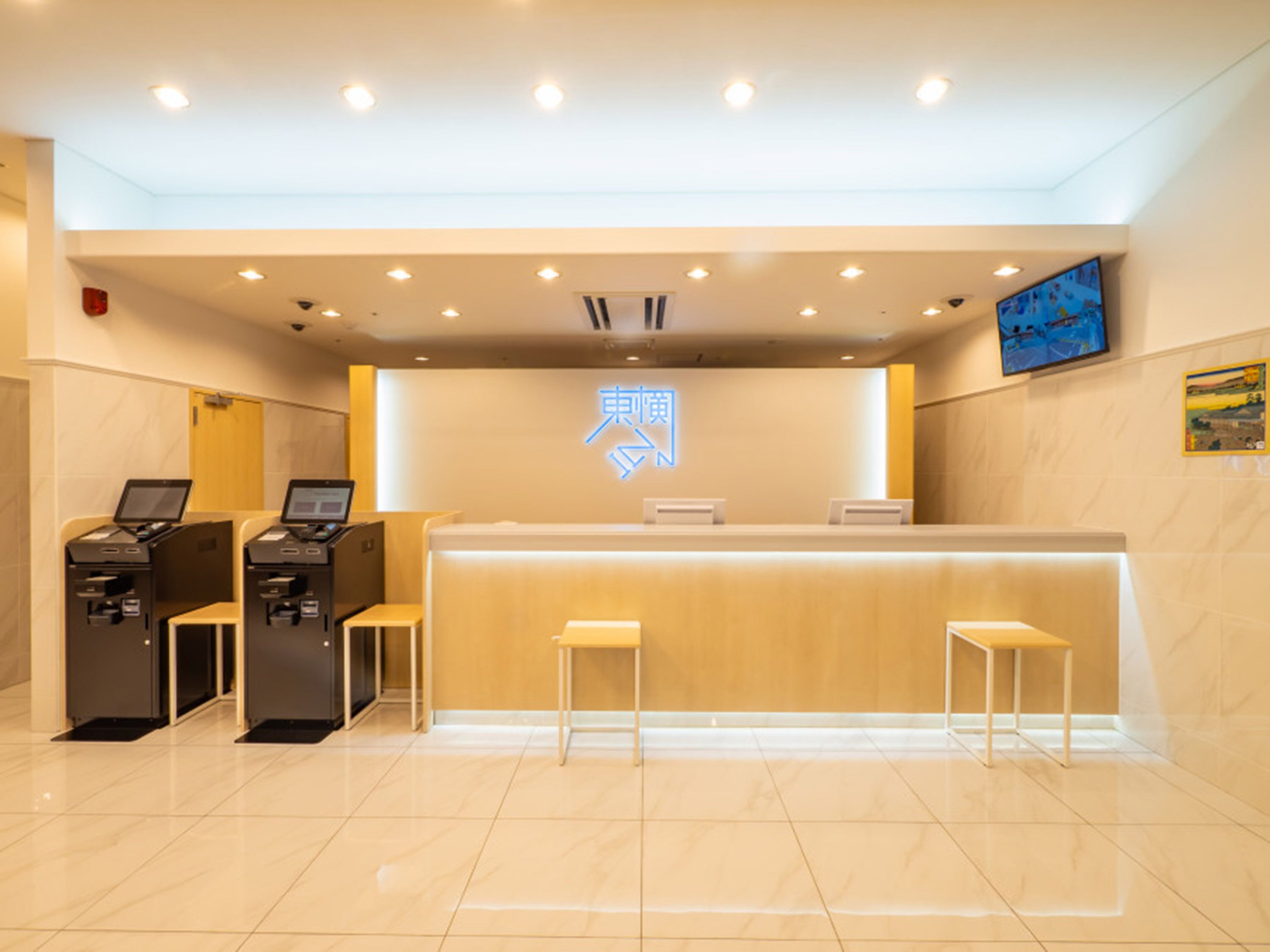 Una zona de recepción con mostrador, dos estaciones de trabajo con computadoras y un letrero de neón.