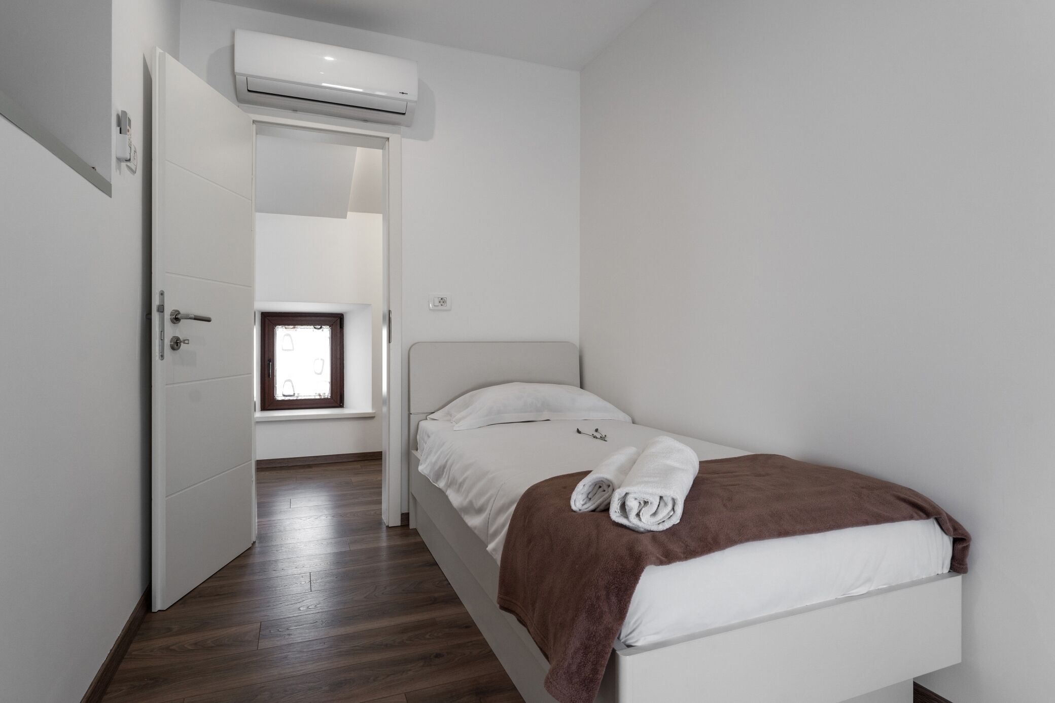 Een kleine, schone kamer met een bed, een raam en een airconditioning.